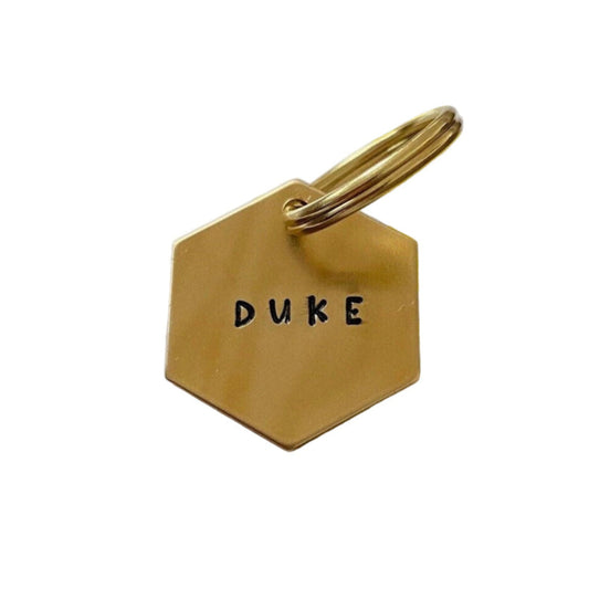 Gold brass dog tag with 'DUKE' stampled on a white background