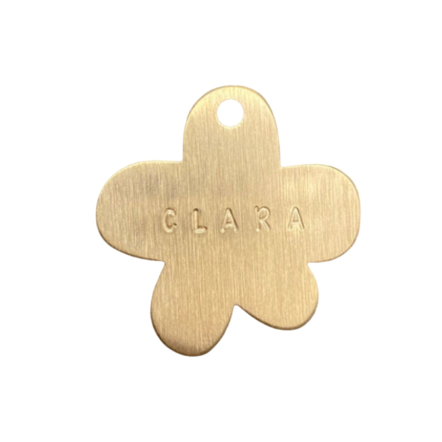 Gold flower-shaped tag with 'CLARA' engraved on a white background