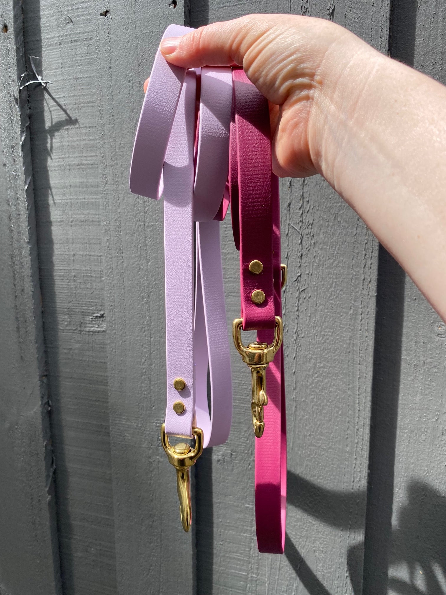 Lavender (purple) and Maroon dog leashes with gold brass hardware held by a hand on a gray surface