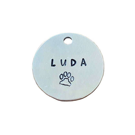 Round metal tag with 'LUDA' and a paw print 